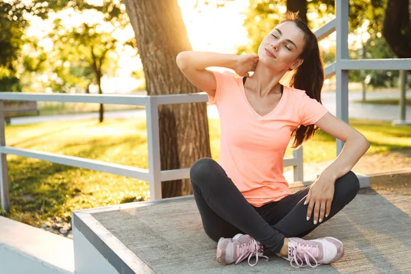 Imagen de chica bonita de fitness sentada en el campo de deportes con las piernas cruzadas por la mañana — Foto de Stock