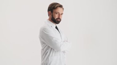 Beyaz profesyonel ceket mutlu genç sakallı adam doktor yan görünümü gülümseyerek ve gri arka plan izole üzerinde kameraya bakarken jest kadar başparmak gösteren