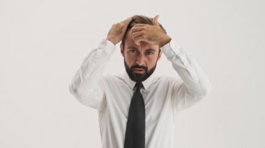 Concentrated young bearded business man becoming happy after fixing his hair and tie over gray background isolated