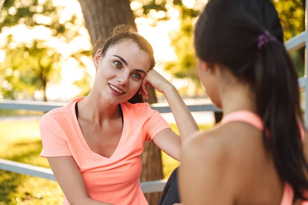 Beeld van aantrekkelijke fitness vrouwen in sportkleding praten samen terwijl zittend in Green Park — Stockfoto