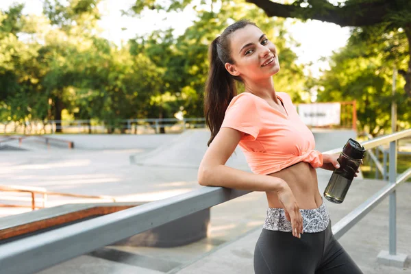 Bild der hübschen Fitness-Mädchen in Sportbekleidung lächelnd und mit Wasserflasche auf dem Sportplatz — Stockfoto