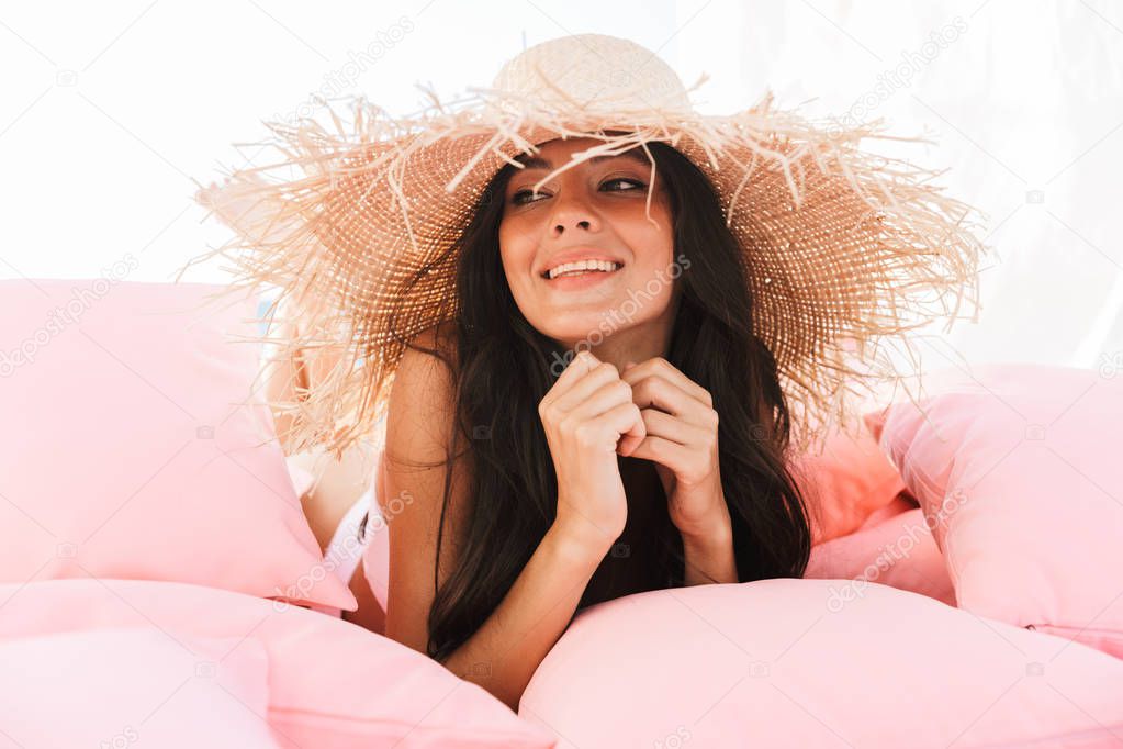 Image of pleased young woman in swimsuit and straw hat smiling w