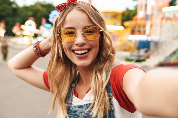 Glad lycklig ung blond kvinna i nöjespark ta Selfie av kamera. — Stockfoto