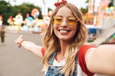 Eğlence parkında neşeli mutlu genç sarışın kadın kamera ile selfie çekmek.