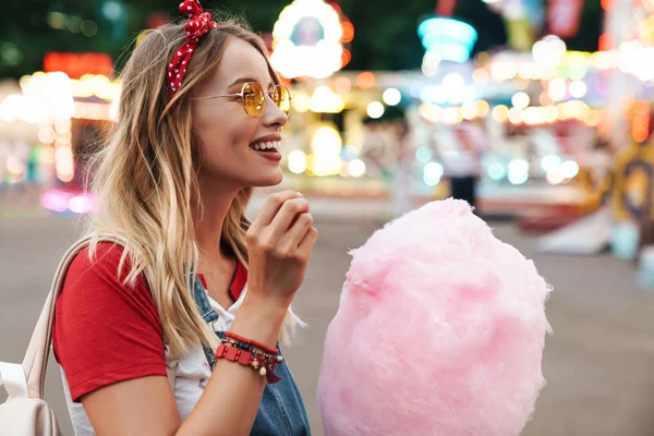 Зображення блондинки красива жінка їсть солодку бавовняну цукерку в той час як — стокове фото