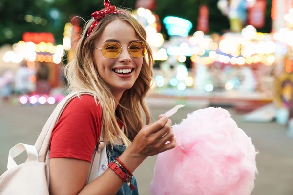 Beeld van positieve blonde vrouw het eten van zoete suikerspin terwijl w — Stockfoto