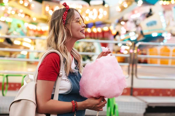 Immagine di donna caucasica bionda che mangia zucchero filato dolce mentre — Foto Stock