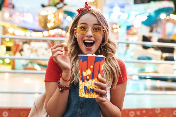 Bild einer süßen blonden Frau, die lächelt und Popcorn in der Hand hält — Stockfoto