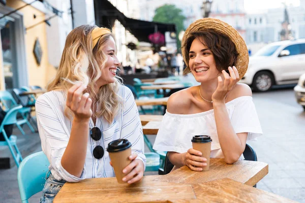 Ευτυχισμένο νεαρό θετικό αισιόδοξα κορίτσια φίλους κάθονται σε εξωτερικούς χώρους στο καφέ πίνοντας καφέ μιλάει μεταξύ τους. — Φωτογραφία Αρχείου