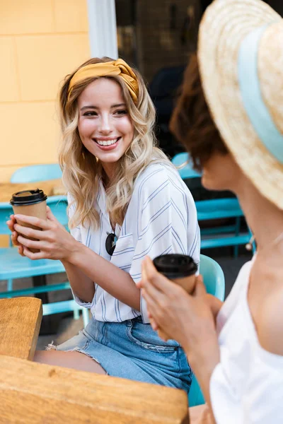 Fröhliche junge positiv optimistische Freundinnen sitzen draußen im Café und trinken Kaffee und reden miteinander. — Stockfoto
