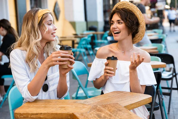 快乐年轻积极乐观女孩朋友坐在户外的咖啡馆喝咖啡互相交谈. — 图库照片