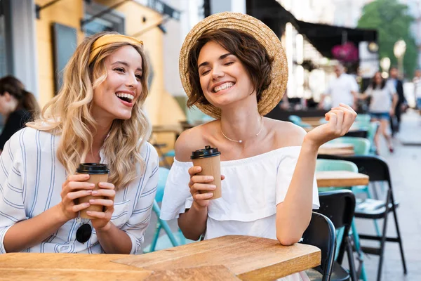 Feliz joven positivo chicas optimistas amigos sentados al aire libre en la cafetería beber café hablando entre sí . — Foto de Stock