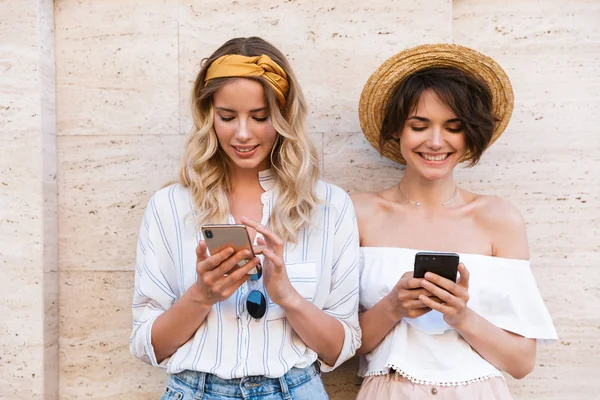Mosolygó elégedett boldog fiatal nők barátai szabadban használ mobiltelefonok csevegni. — Stock Fotó
