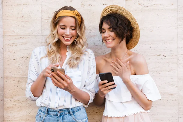 Glimlachend blij gelukkig positief jonge vrouwen vrienden buitenshuis met behulp van mobiele telefoons chatten. — Stockfoto