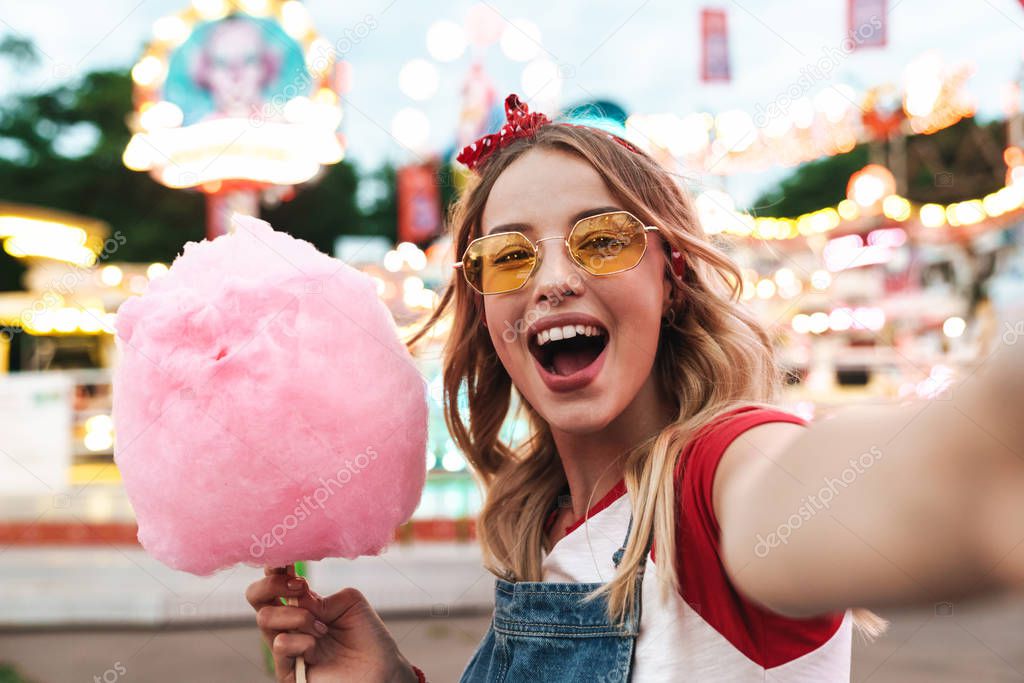 Image of excited blonde woman holding sweet cotton candy while t