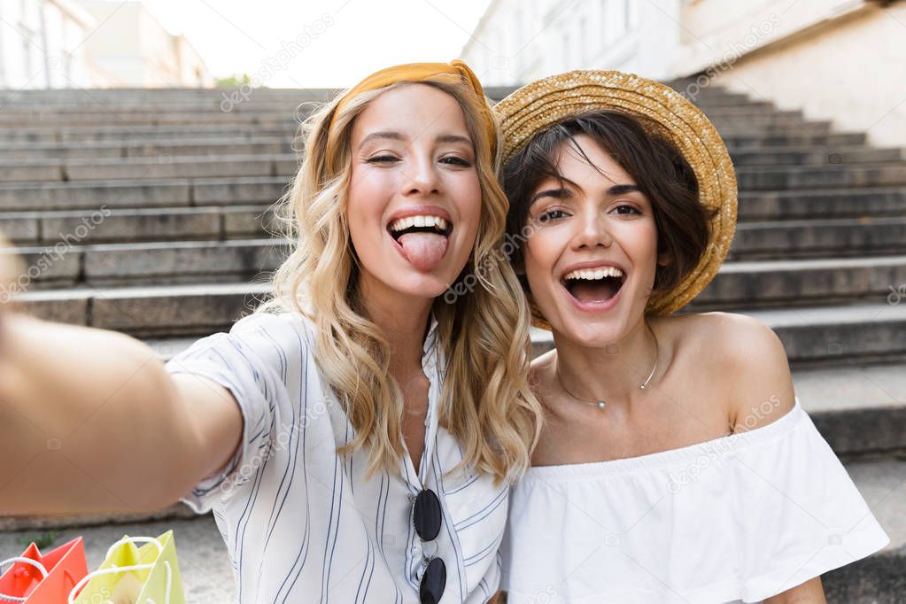 Smiling cute young girls friends outdoors on steps take a selfie by camera.