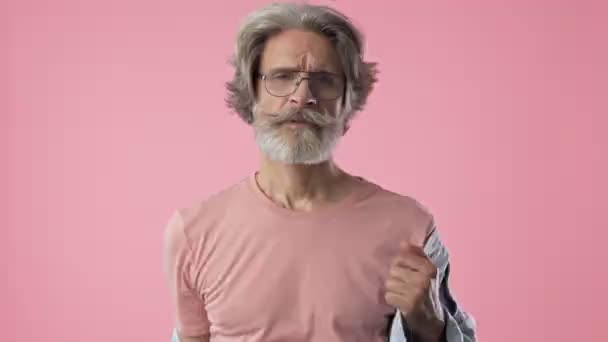 自信的年长时尚胡子男子与灰色的头发穿着牛仔夹克 同时看着相机在粉红色背景隔离 — 图库视频影像
