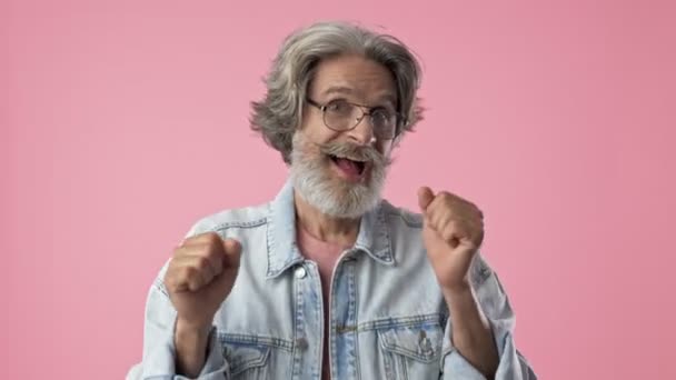兴奋的老人时尚胡子男子与灰色的头发在牛仔夹克跳舞和手势与手在粉红色背景孤立 — 图库视频影像