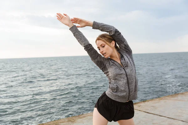 Sabah deniz kenarındaki iskelede çalışırken egzersiz yapan baştan çıkarıcı sportif kadın görüntüsü — Stok fotoğraf