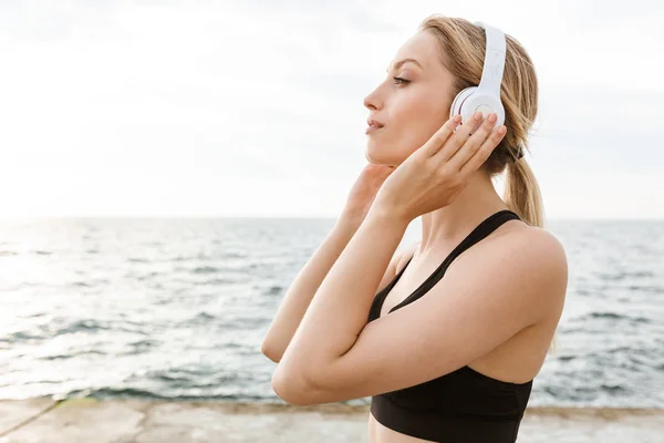 Imagen de una hermosa mujer tranquila escuchando música con auriculares cerca de la playa en la mañana — Foto de Stock