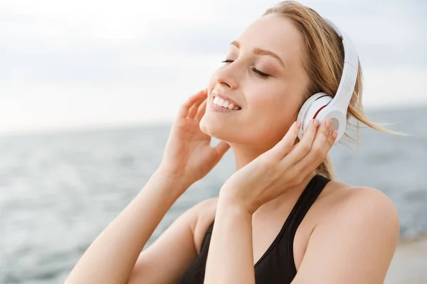 Beeld van gelukkige mooie vrouw luisteren naar muziek met koptelefoon in de buurt van Seaside in de ochtend — Stockfoto