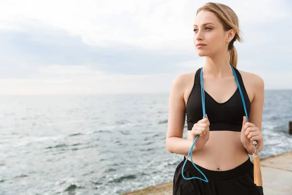 Beeld van aantrekkelijke vrouw staande met springen touw over de nek terwijl het trainen in de buurt van Seaside in de ochtend — Stockfoto