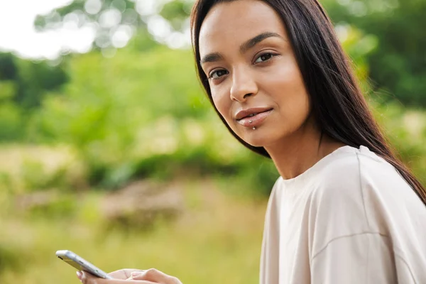 Retrato de mulher adorável usando lábio piercing segurando smartphone no parque verde — Fotografia de Stock