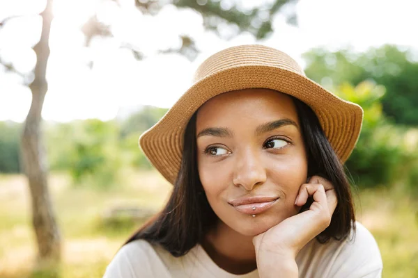 Foto da linda mulher usando chapéu de palha olhando para o lado enquanto caminhava no parque verde — Fotografia de Stock