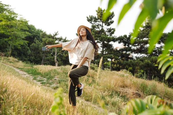 Foto di donne compiaciute che ballano e ascoltano musica sul cellulare mentre camminano nel parco verde — Foto Stock