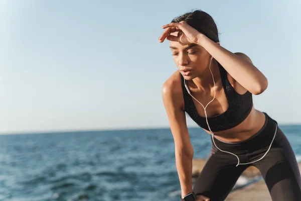 Ernst schöne junge starke Sportlerin draußen am Strand am Morgen eine Pause haben Musik hören mit Kopfhörern. — Stockfoto