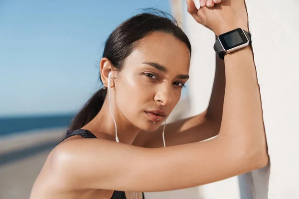 Ziemlich schöne ernsthafte starke Sportlerin draußen am Strand am Morgen Musik hören mit Kopfhörern. — Stockfoto