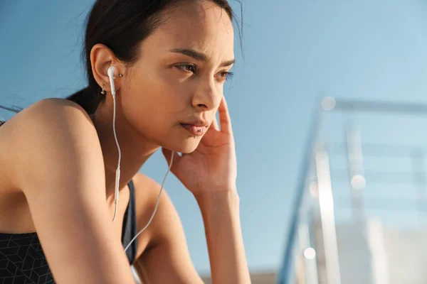 Bastante hermosa mujer deportiva seria fuerte al aire libre en la playa por la mañana escuchando música con auriculares . — Foto de Stock