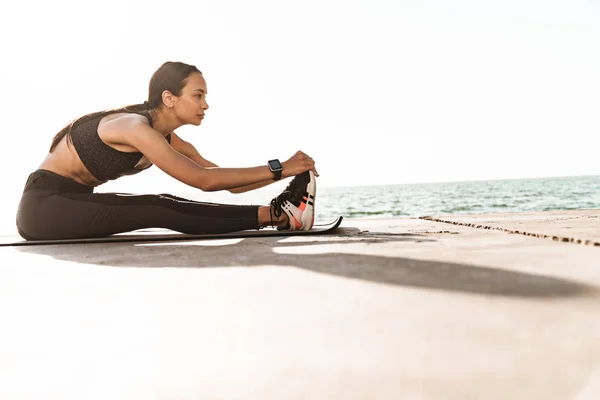 Fiatal erős fitness nő a szabadban, a tengerparton, reggel, hogy Stretching gyakorlatok. — Stock Fotó