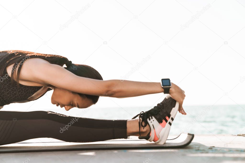 Young strong fitness woman outdoors at the beach at morning make stretching exercises.