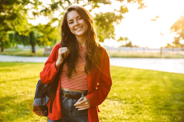 Imagem de menina agradável estudante sorrindo e olhando para a câmera enquanto caminhava no parque verde — Fotografia de Stock