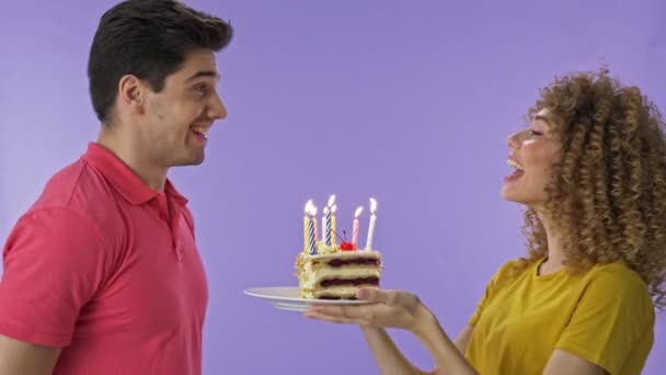 欢快的年轻女子祝贺她的男朋友的生日蛋糕 英俊的年轻人变得很高兴 吹出他的生日蛋糕上的蜡烛 有吸引力的年轻可爱的夫妇庆祝生日与蛋糕 — 图库视频影像