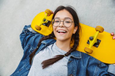 Beton duvar üzerinde kaykay tutarken gülümseyen ve sevinçli sevimli kız Görüntü