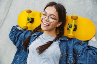 Beton duvar üzerinde kaykay tutarken neşeli kız gülümseyen ve sevinçli Görüntü