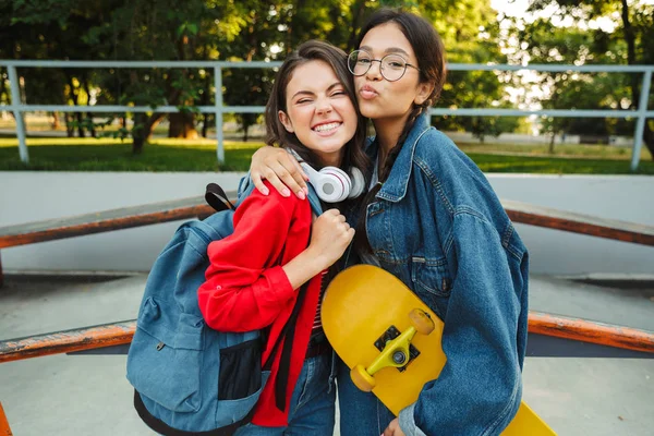 Immagine di due ragazze carine che sorridono e si abbracciano mentre tengono lo skateboard nello skate park — Foto Stock