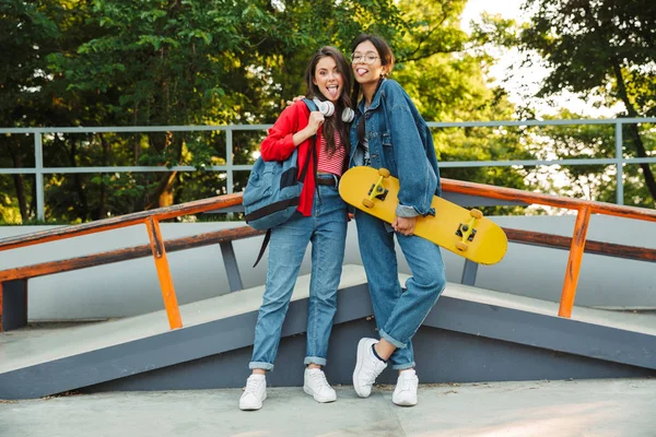 Immagine di due ragazze gioiose che sporgono la lingua e si abbracciano mentre tengono lo skateboard nello skate park — Foto Stock