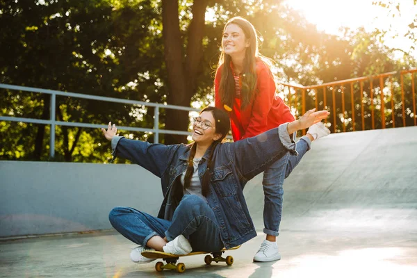 Imagem de duas meninas felizes rindo e andando de skate juntos no parque de skate — Fotografia de Stock