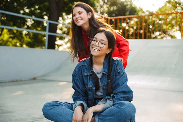 Image of two pretty girls laughing and riding skateboard together in skate park — Stock Photo, Image