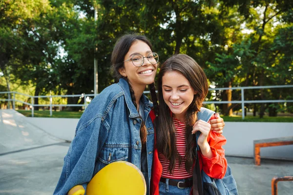 Image de deux filles ravies souriant et se câlinant ensemble tout en tenant skateboard dans le skate park — Photo