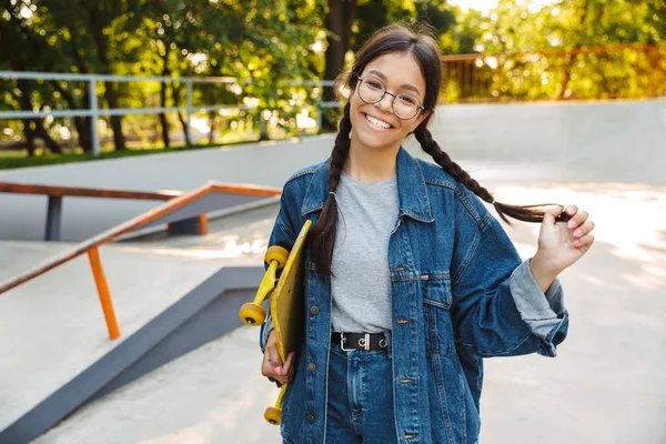 스케이트 공원에서 스케이트 보드를 들고있는 동안 웃고 기뻐하는 백인 소녀의 이미지 — 스톡 사진