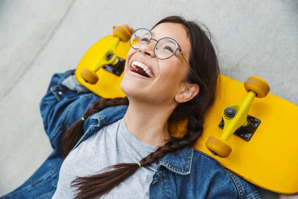 Image de fille heureuse riant et se réjouissant tout en tenant skateboard sur le mur de béton — Photo