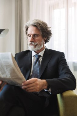 Konsantre yakışıklı gri saçlı üst düzey işadamı evde resmi kıyafetler gazete okuma giymiş kapalı.