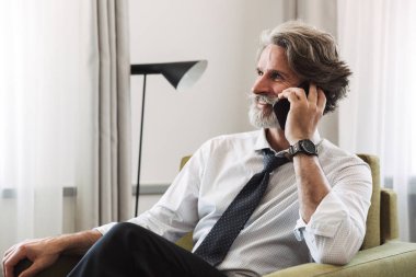 Otururken cep telefonuyla konuşan mutlu olgun adamın görüntüsü 