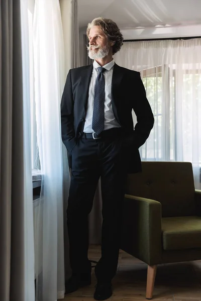 Bärtige reife gutaussehende grauhaarige Geschäftsmann posiert zu Hause in der Nähe des Fensters in formeller Kleidung. — Stockfoto