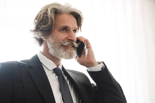 Konzentrierter seriöser, gutaussehender, grauhaariger Geschäftsmann zu Hause in formeller Kleidung, der mit einer Handytasche spricht. — Stockfoto