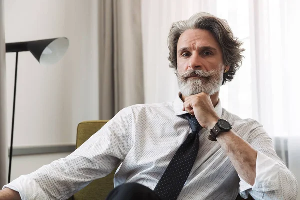 Image of masculine mature man wearing suit and tie sitting on ar